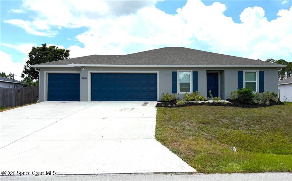 Contemporary stucco exterior featuring a three-car garage with matching garage doors, a front entry, and a landscaped garden bed