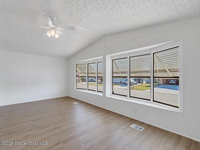 Empty room with ceiling fan, light wood-style floors, and vaulted ceiling
