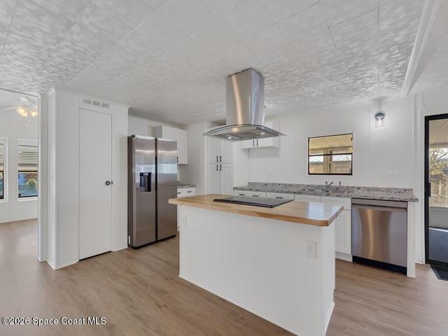 Kitchen with plenty of natural light, butcher block counters, island exhaust hood, and white cabinetry