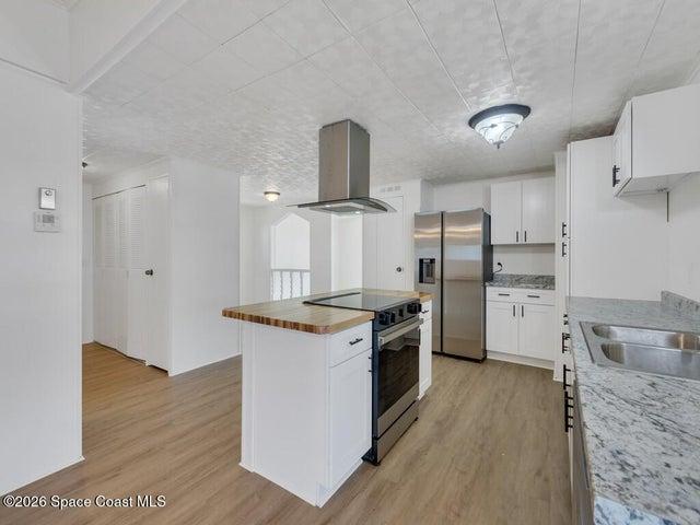 Kitchen with a kitchen island, island range hood, stainless steel appliances, butcher block countertops, and white cabinets