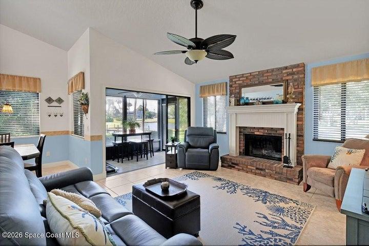 Bright & inviting living room featuring vaulted ceilings and abundant natural light. The space is anchored by a charming brick wood burning fireplace with a classic white mantel, creating a warm focal point.