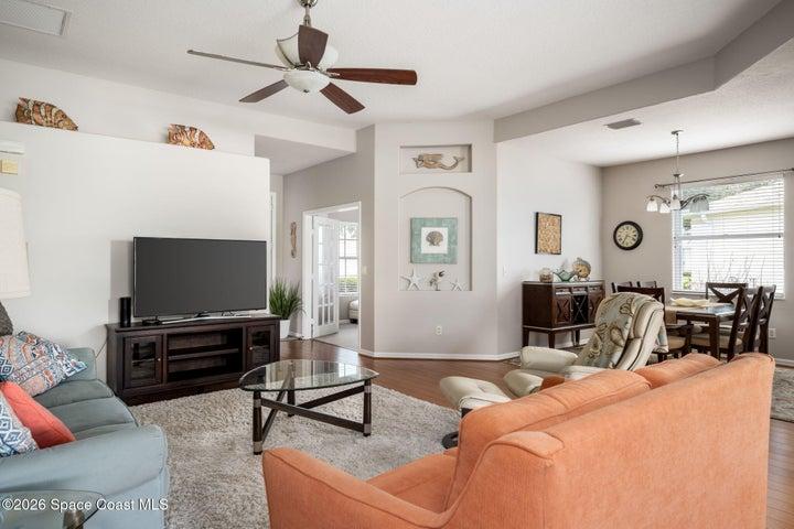 Spacious living room area featuring wood-finish flooring, a ceiling fan, and beautiful natural light
