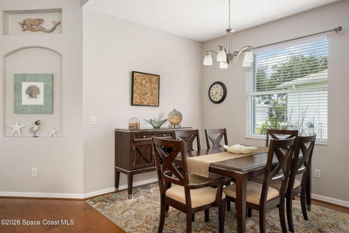 Formal dining space off of living room features wood-finish flooring, a contemporary chandelier, with ample natural light from a window with blinds
