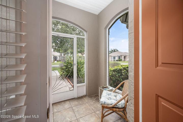 Tiled front entry featuring an arched sidelight, a full-lite screen door with decorative wrought iron, and an interior wood shutter