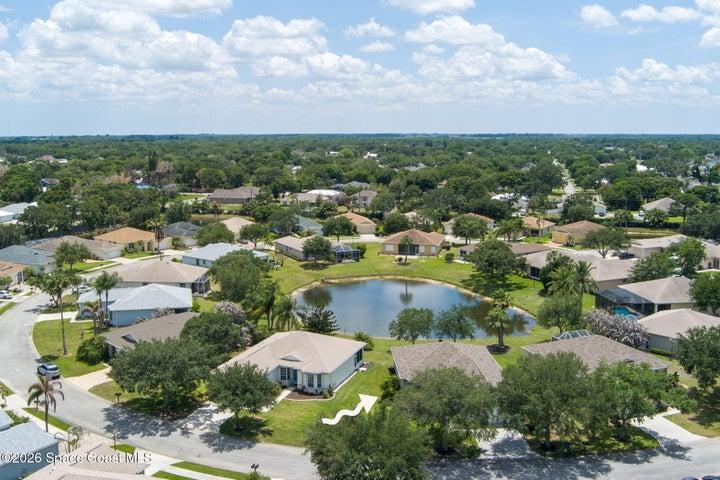 Aerial perspective showcasing a residential community with numerous single-family homes, a central pond, and abundant mature trees