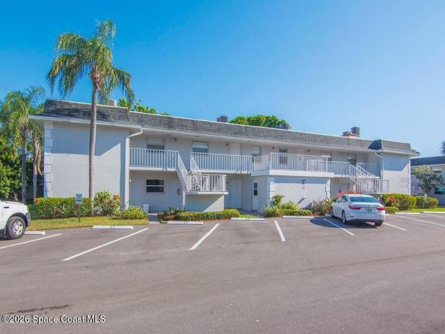 Multi-story building featuring stucco exterior, multiple balconies with white railings, and a parking lot with marked spaces