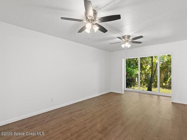 Spacious room featuring wood-finish flooring, white walls, and a large window overlooking lush greenery