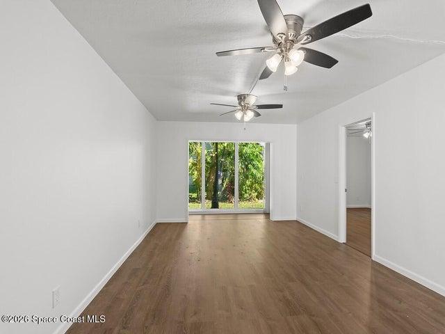 Spacious interior room featuring wood-finish flooring, white walls, and two ceiling fans with integrated lighting
