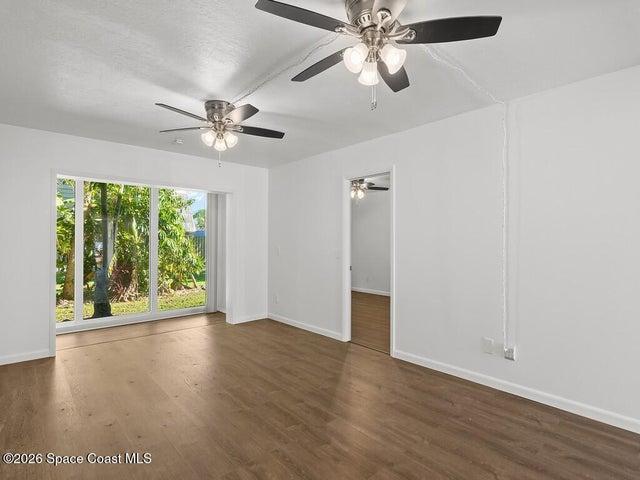 Spacious room featuring wood-finish flooring, white walls, and two ceiling fans with integrated lighting
