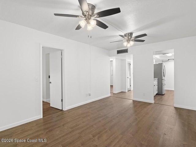 Spacious room featuring wood-finish flooring, white walls, and two ceiling fans with integrated lighting