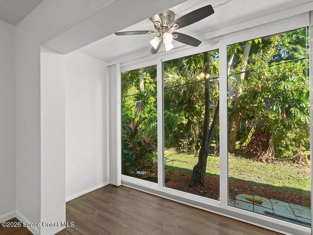Room featuring wood-finish flooring, a ceiling fan with integrated lighting, and expansive glass panels overlooking a lush exterior