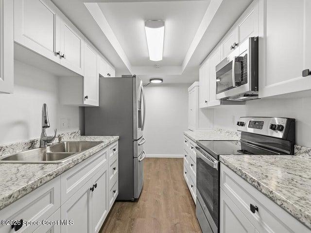 Galley kitchen featuring white shaker cabinetry, light granite-look countertops, and wood-finish flooring
