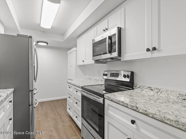 Modern kitchen featuring white shaker cabinetry, stainless steel appliances, speckled countertops, and wood-finish flooring