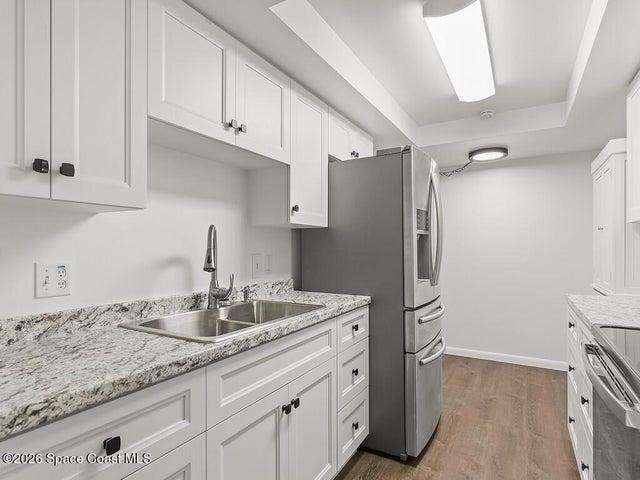 Modern kitchen featuring white shaker cabinetry, speckled countertops, a stainless steel double basin sink with a gooseneck faucet, and wood-finish flooring