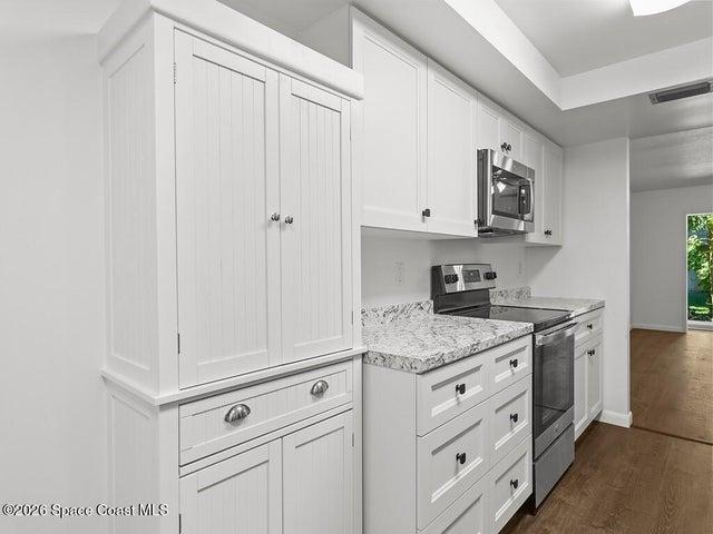 Contemporary kitchen featuring white cabinetry with black hardware, stainless steel appliances, granite-look countertops, and wood-finish flooring