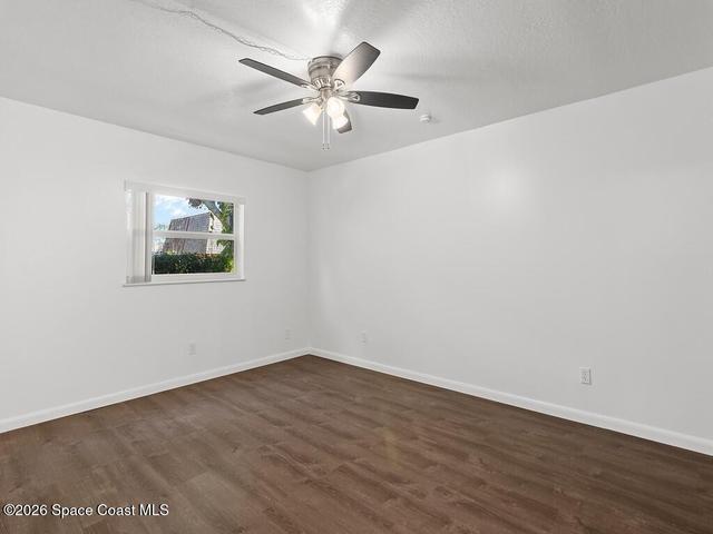 Room featuring wood-finish flooring, white painted walls, a single window, and a ceiling fan with integrated lighting