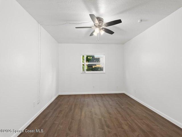 Spacious room featuring wood-finish flooring, white walls, and a ceiling fan with integrated lighting