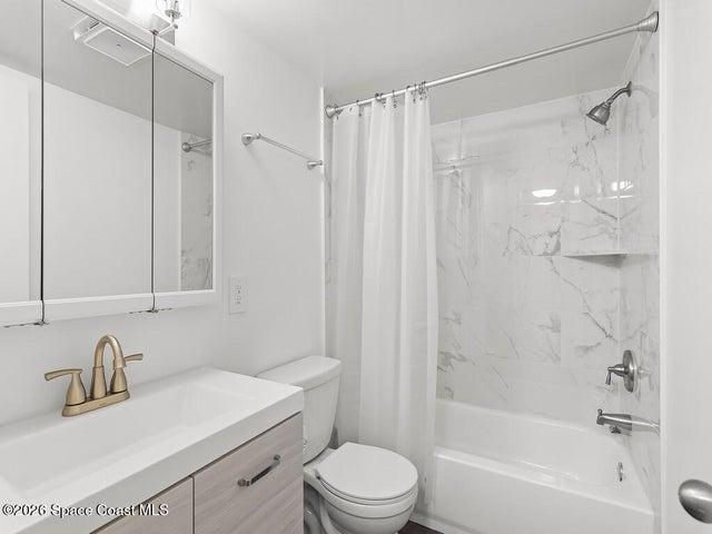 Bathroom featuring a vanity with integrated sink and brushed gold faucet, a wall-mounted mirrored medicine cabinet, a toilet, and a combination tub/shower with white subway tile surround