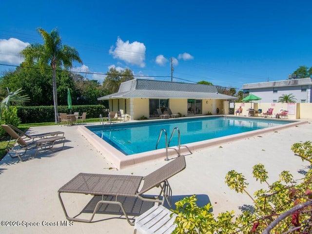 Expansive swimming pool area featuring a rectangular pool with light-colored coping, a surrounding concrete deck, and mature tropical landscaping