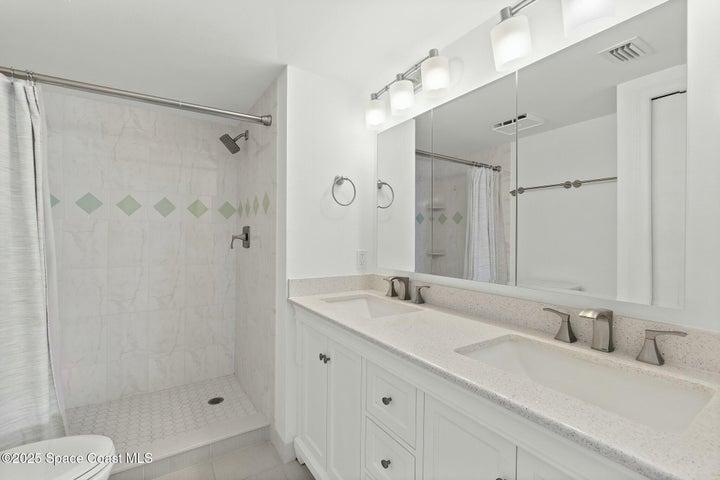 Primary bathroom with dual sink vanity, quartz countertop, and walk-in tile shower