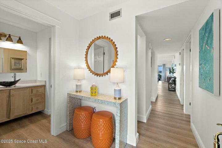 Entry foyer with powder bath, round mirror, console table, and wood-look flooring, Cocoa Beach condo