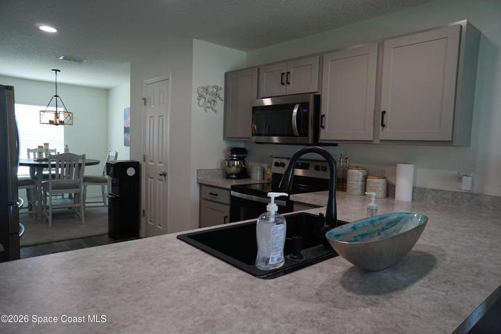 Kitchen featuring light grey cabinetry with black hardware, stainless steel appliances, and a black sink with a gooseneck faucet