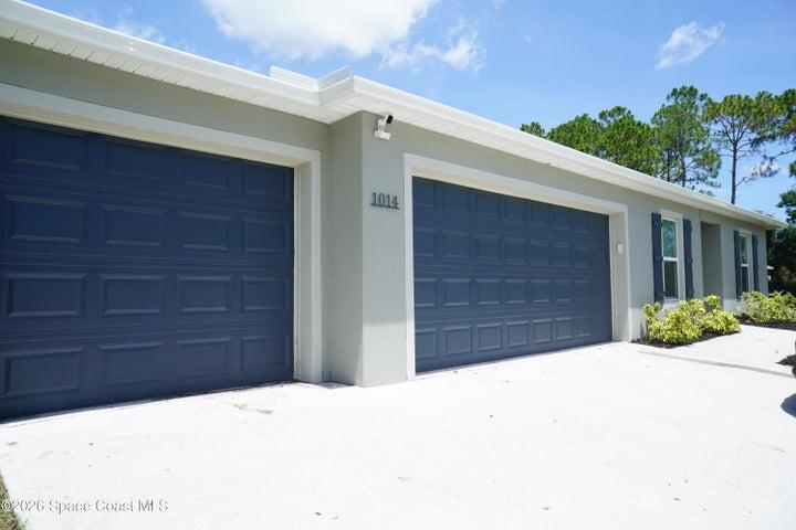 Two dark panel garage doors on a light gray stucco exterior with white trim