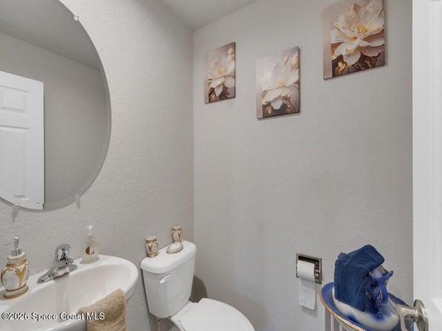Powder room featuring a pedestal sink, chrome faucet, and a round wall-mounted mirror