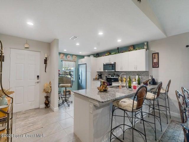 Contemporary kitchen featuring a granite-topped island with seating, white shaker-style cabinetry, recessed lighting, and stainless steel appliances