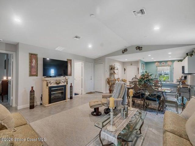 Open-concept living space featuring a decorative fireplace surround, tiled flooring, vaulted ceiling, recessed lighting, and a defined dining area