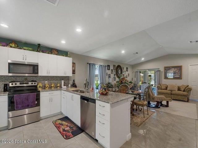 Open-concept kitchen featuring white cabinetry, stainless steel appliances, granite countertops, and tile flooring