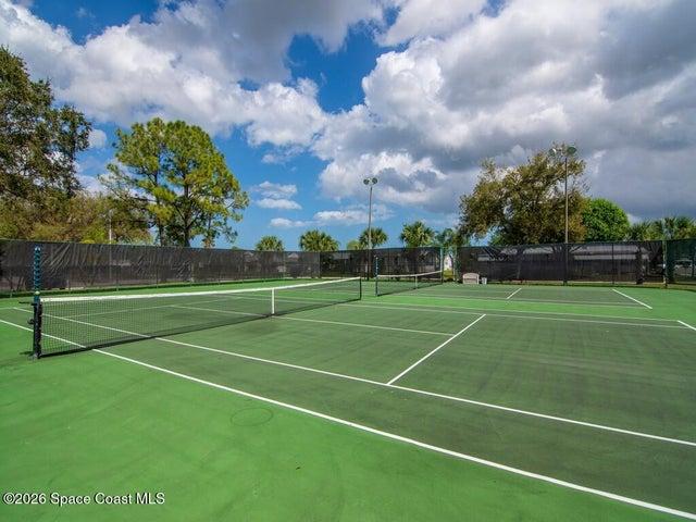Two professional-grade tennis courts featuring a green surface, white court lines, and black perimeter fencing