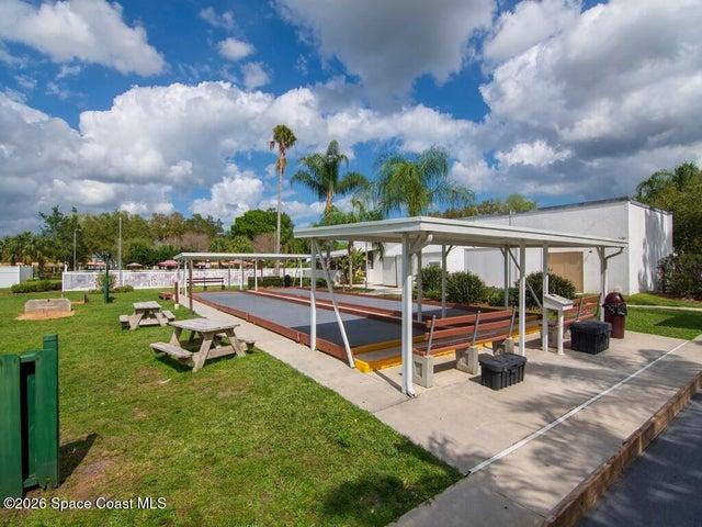 Bocce ball court with covered seating, flanked by manicured green spaces and mature palm trees