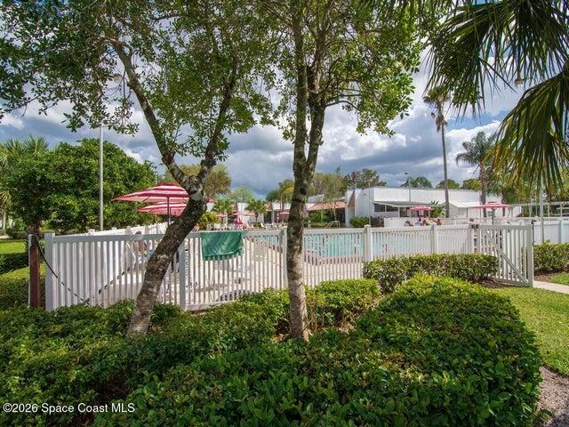 Outdoor pool area featuring a white picket fence, surrounding lush green landscaping, and striped patio umbrellas
