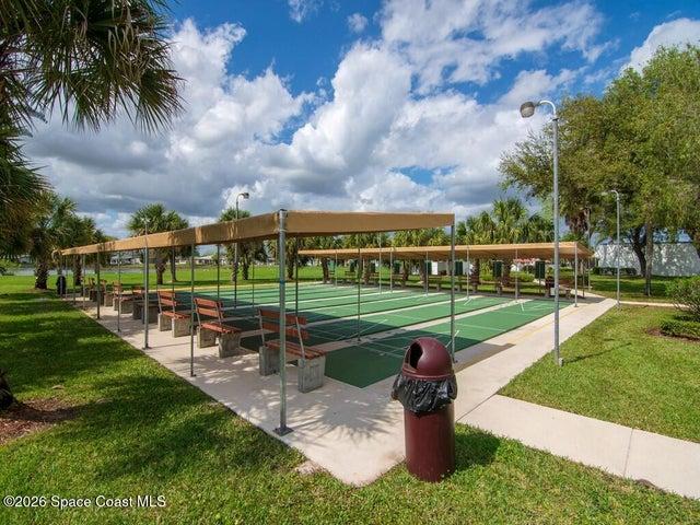 Multiple green shuffleboard courts with white markings, shaded by a long canopy structure