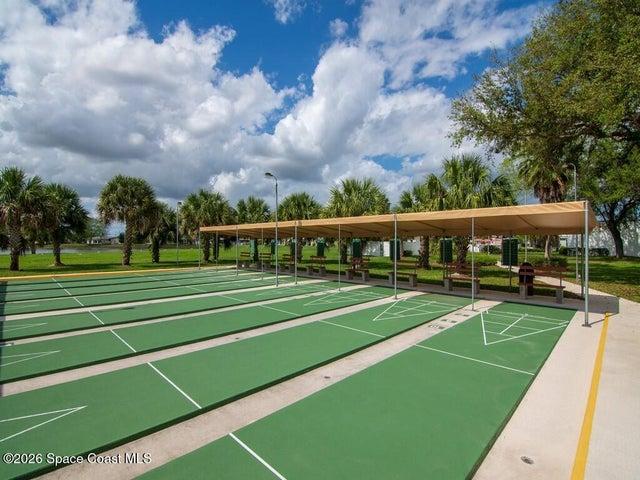 Multiple green shuffleboard courts with white markings, shaded by a long canopy structure