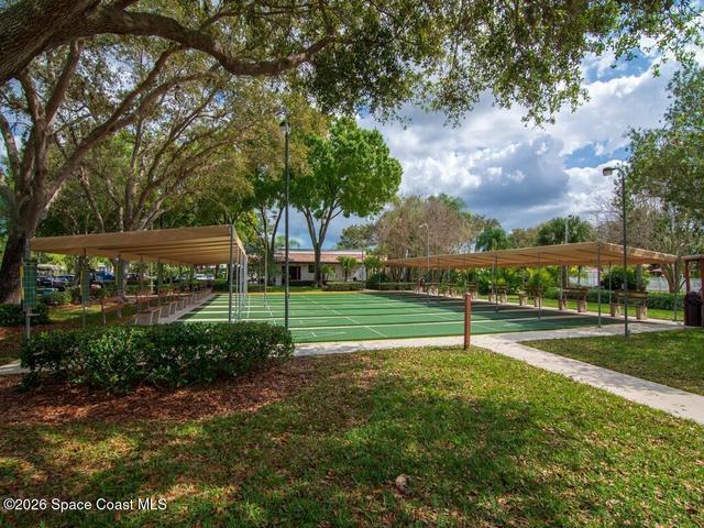 Multiple green shuffleboard courts with white markings, shaded by a long canopy structure