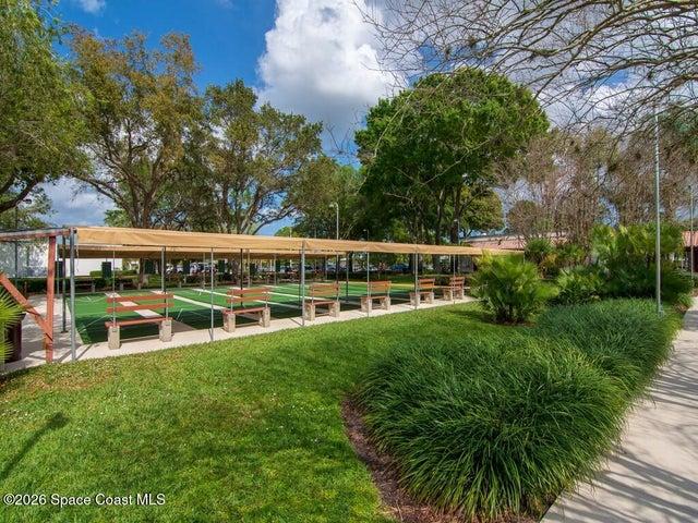 Multiple green shuffleboard courts with white markings, shaded by a long canopy structure