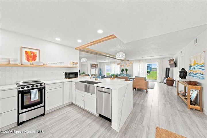 Updated kitchen, featuring white shaker cabinetry, stainless steel appliances, waterfall quartz countertops, and a spacious breakfast bar