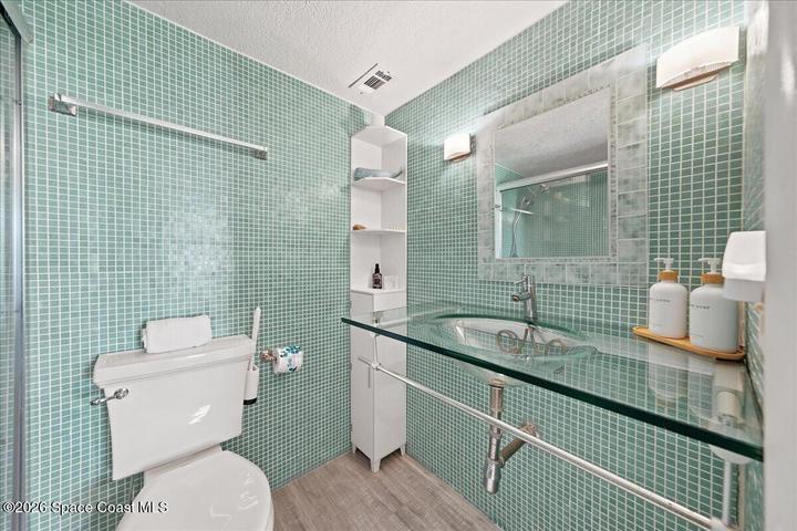 Primary bathroom featuring stunning floor-to-ceiling glass tile, a custom floating glass vanity, contemporary fixtures, and designer finishes that create a luxurious, modern retreat