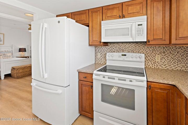 Kitchen with white French-door refrigerator, electric range and granite countertops — Cocoa Beach condo