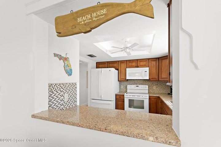 Kitchen pass-through with granite bar seating and coastal decor — Cocoa Beach