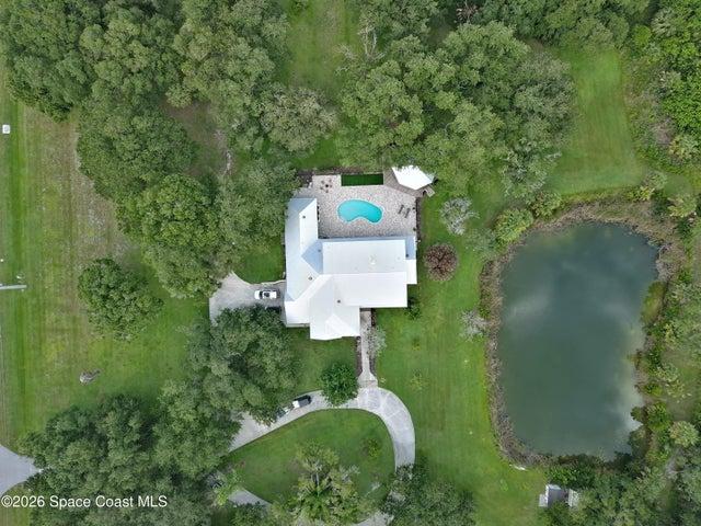Estate-sized parcel featuring a private residence, a freeform swimming pool with a surrounding patio, mature trees, a private pond, and a concrete driveway