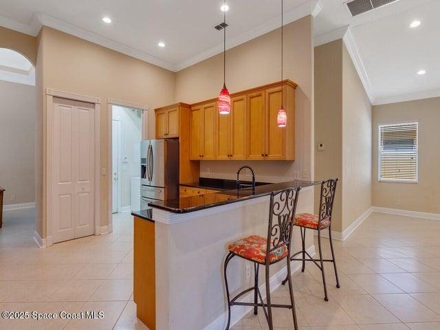 Kitchen with crown molding, a kitchen breakfast bar, decorative light fixtures, light tile patterned flooring, and dark stone countertops