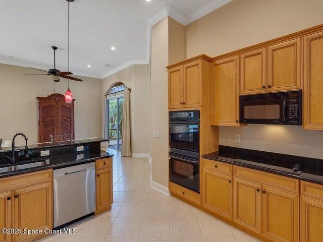 Kitchen featuring black appliances, dark stone counters, crown molding, a ceiling fan, and light tile patterned floors