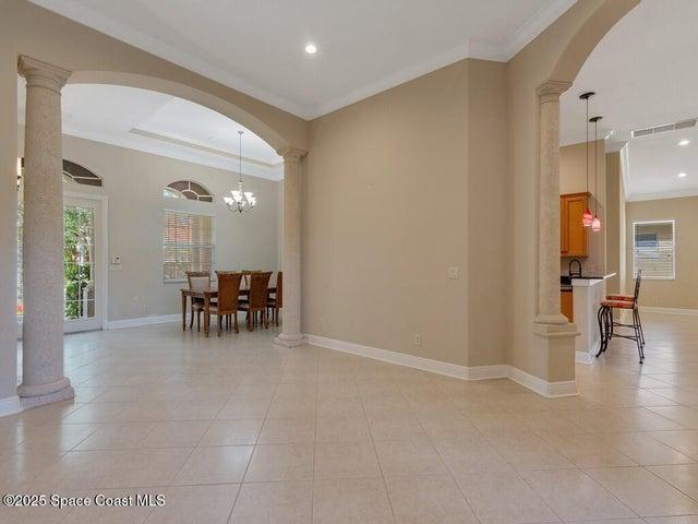 Living room featuring decorative columns, arched walkways, crown molding, recessed lighting, and a chandelier