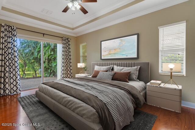 Bedroom with crown molding, light wood-style floors, a tray ceiling, ensuite bathroom, and a ceiling fan