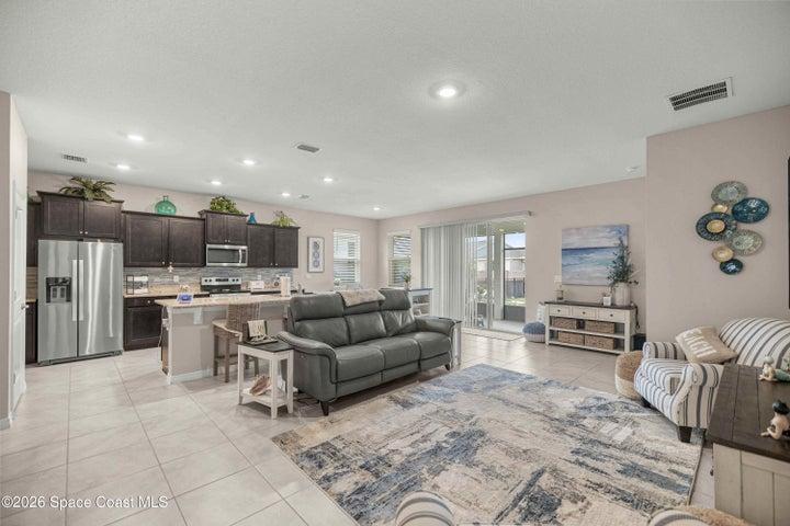 Open-concept living space featuring ceramic tile flooring, recessed lighting, a kitchen with dark wood-finish cabinetry, stainless steel appliances, and a breakfast bar