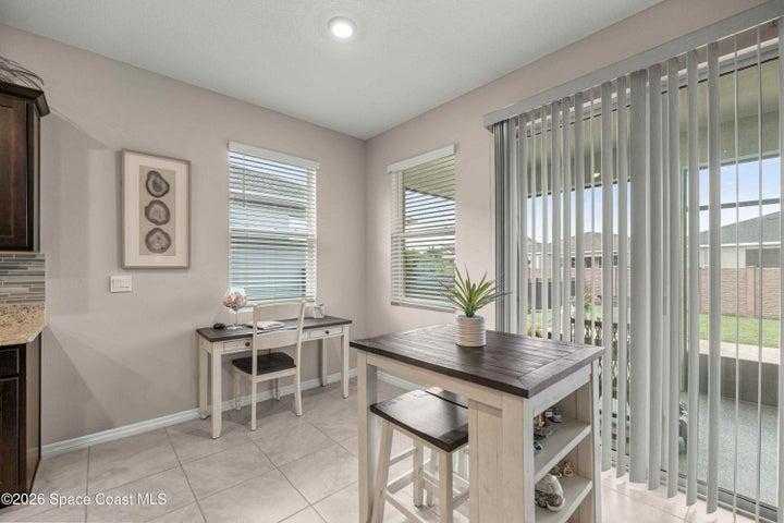 Tiled flooring throughout this bright space, featuring a built-in desk area, a kitchen island with integrated shelving, and vertical blinds covering the sliding glass door