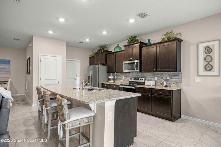 Spacious kitchen featuring an extended island with seating, granite countertops, dark wood-finish cabinetry, stainless steel appliances, and tile flooring